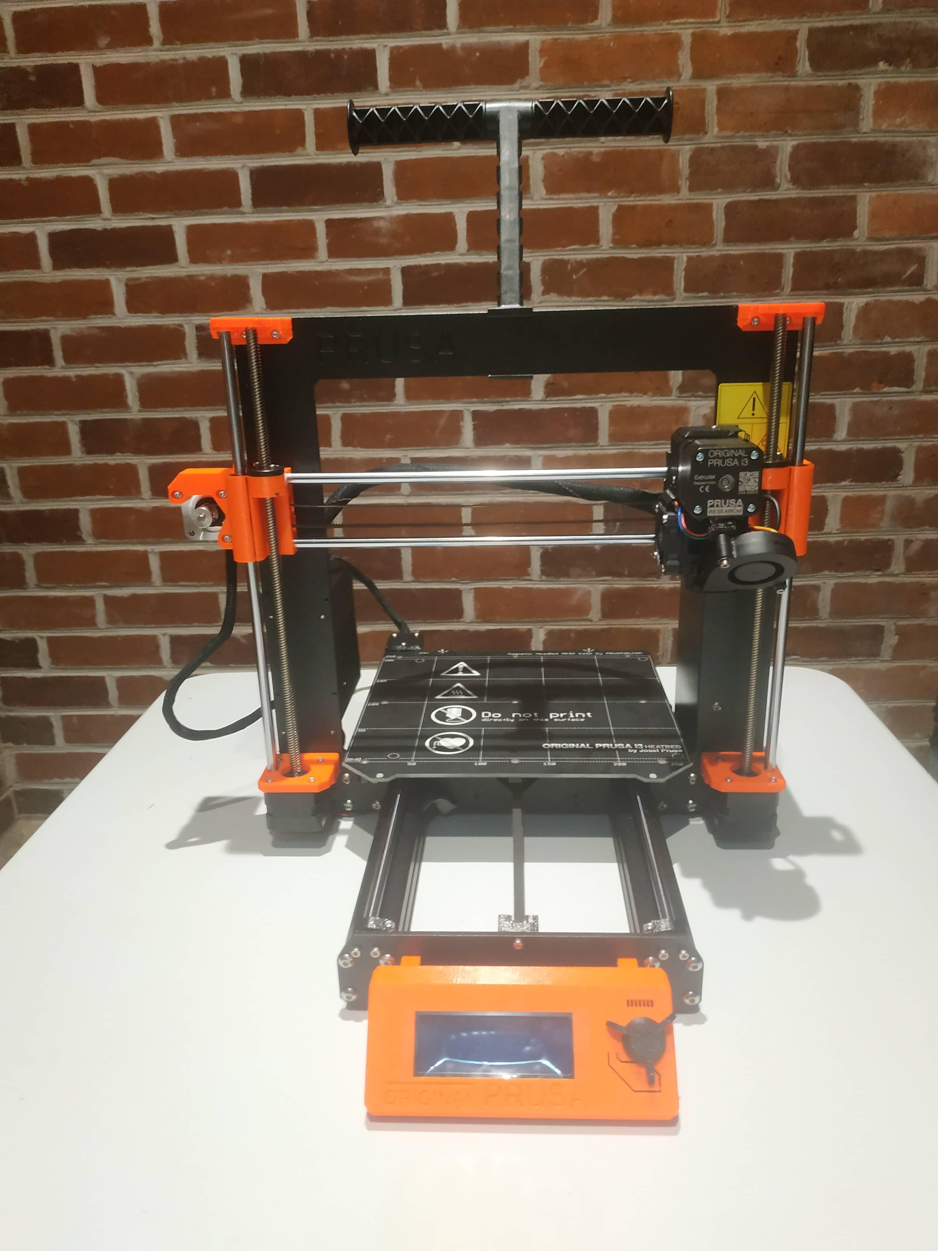 A Prusa brand 3D printer, sporting a black rectangular frame with orange accents
