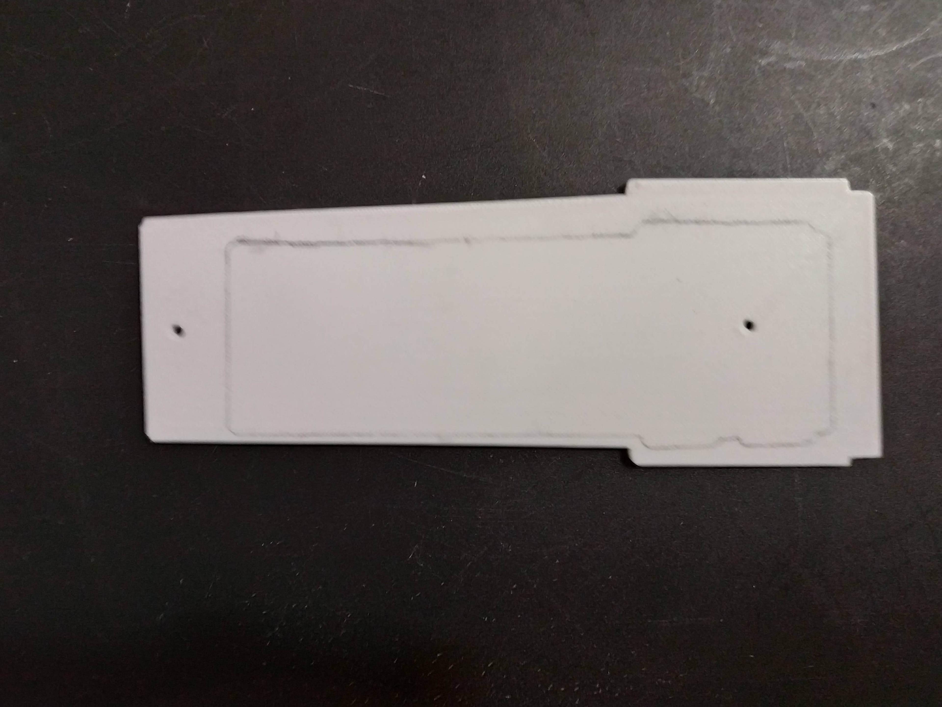 A white plastic part sits on a table. It has two holes for screws, and a pencil outline showing just how far off my design was from fitting