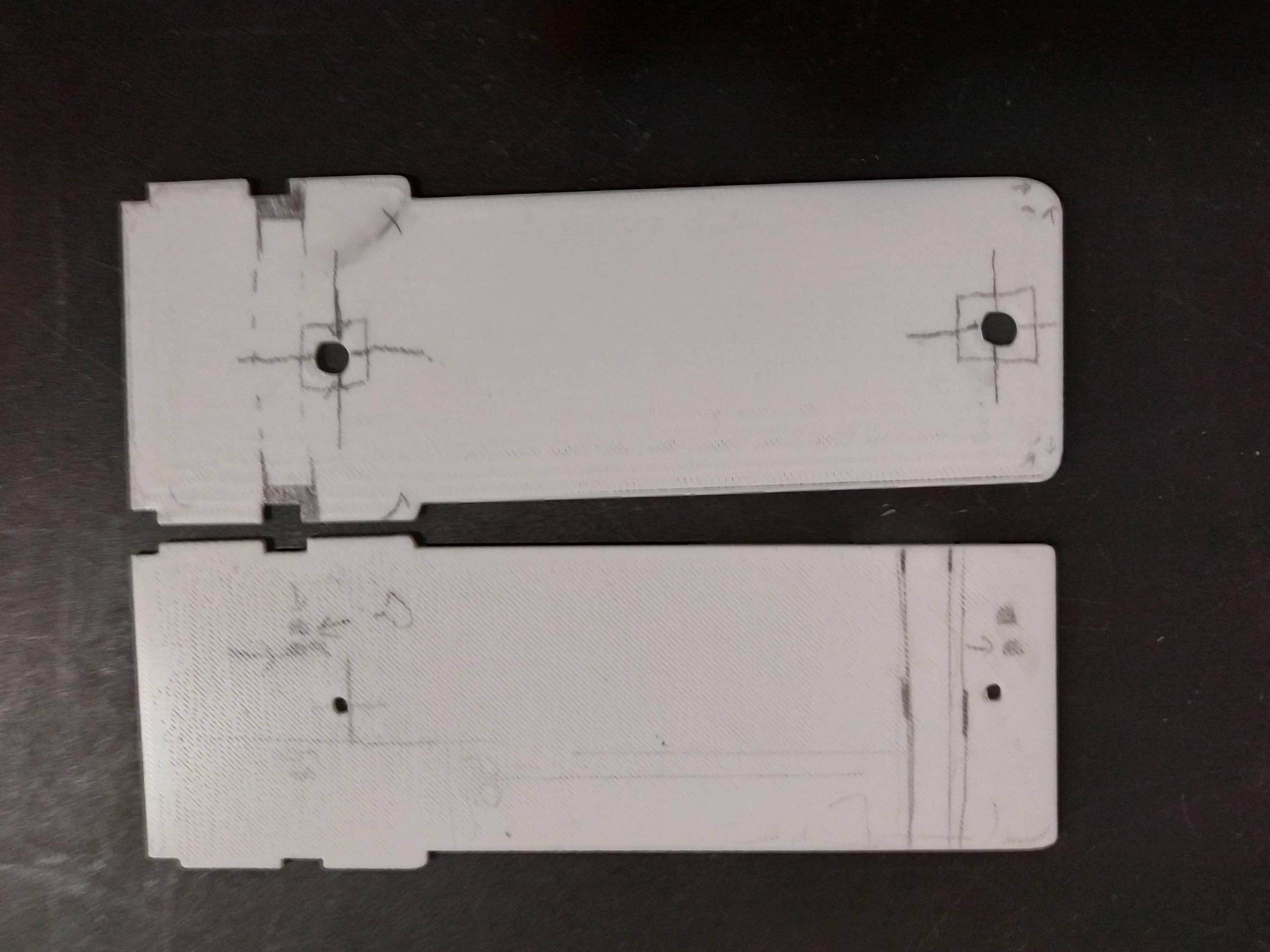 Two white plastic parts side-by-side each other, with pencil markings indicating proposed changes to the design