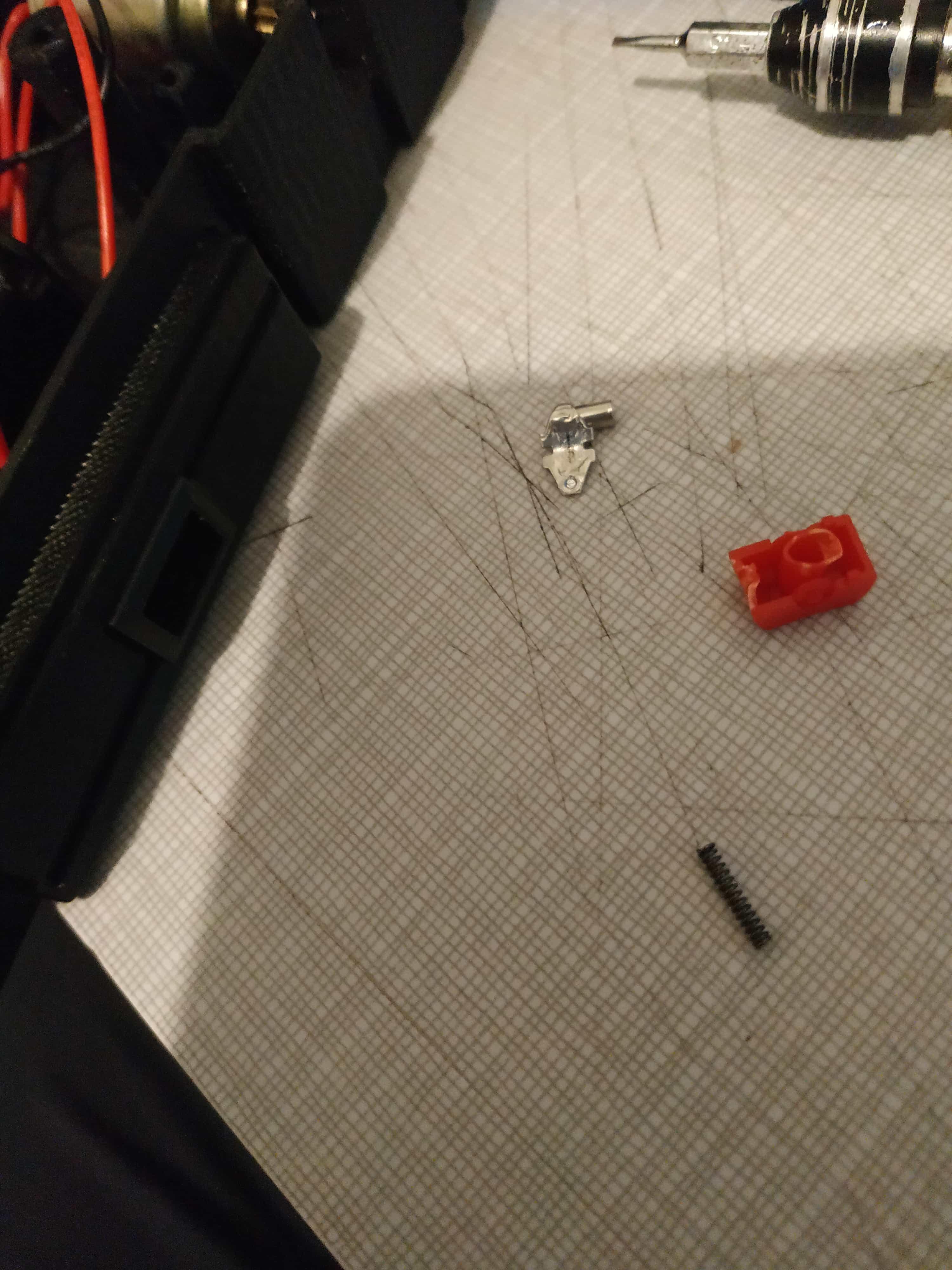 A broken rocker switch lies on a desk. There is a plastic shell, a metal rocker, a spring, and a red piece of plastic that is half-melted