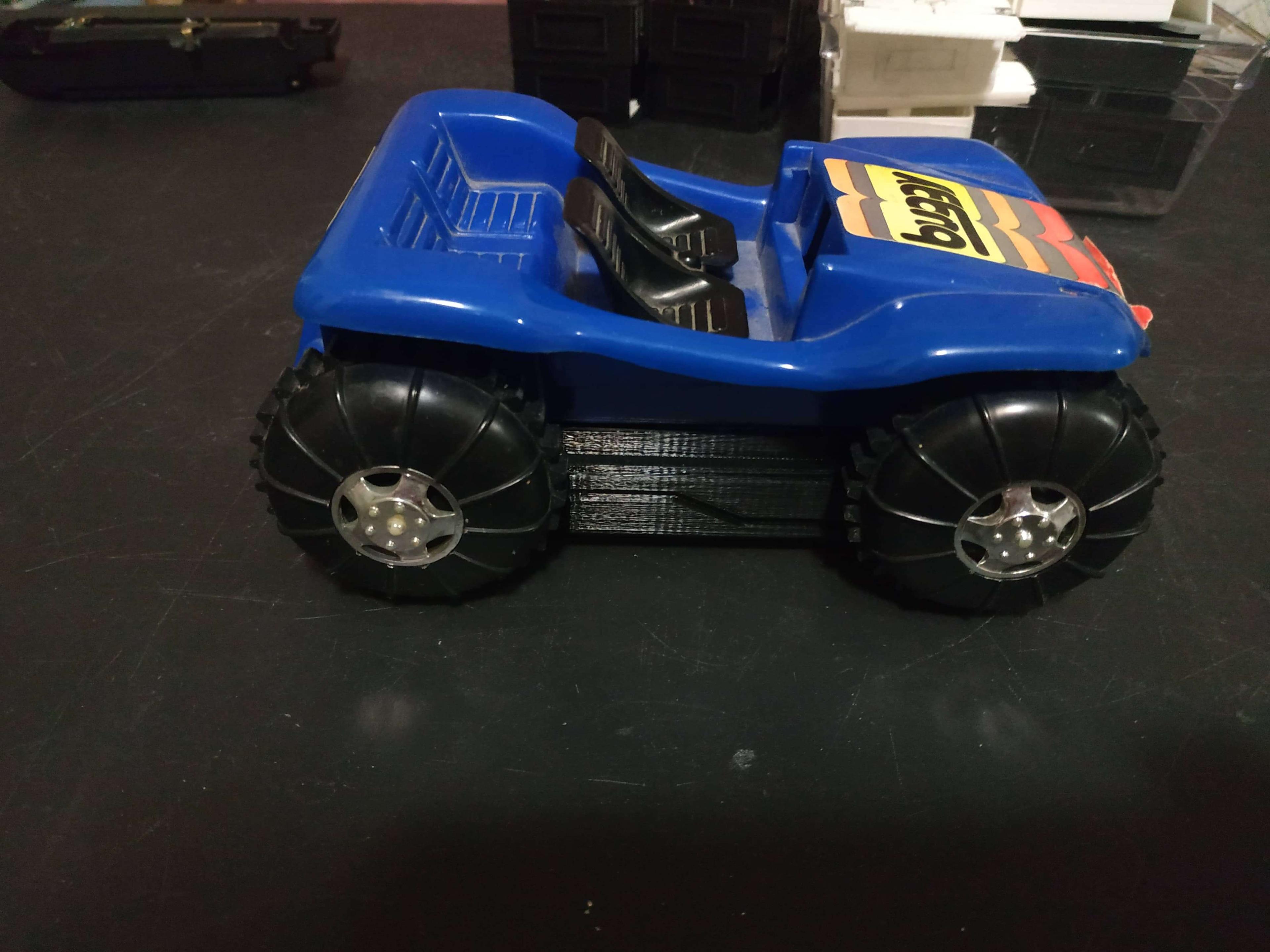 The buggy sits on its wheels on a table, the side opposite the switch is showing, with a 'lightning bolt' pattern on the 3D printed base