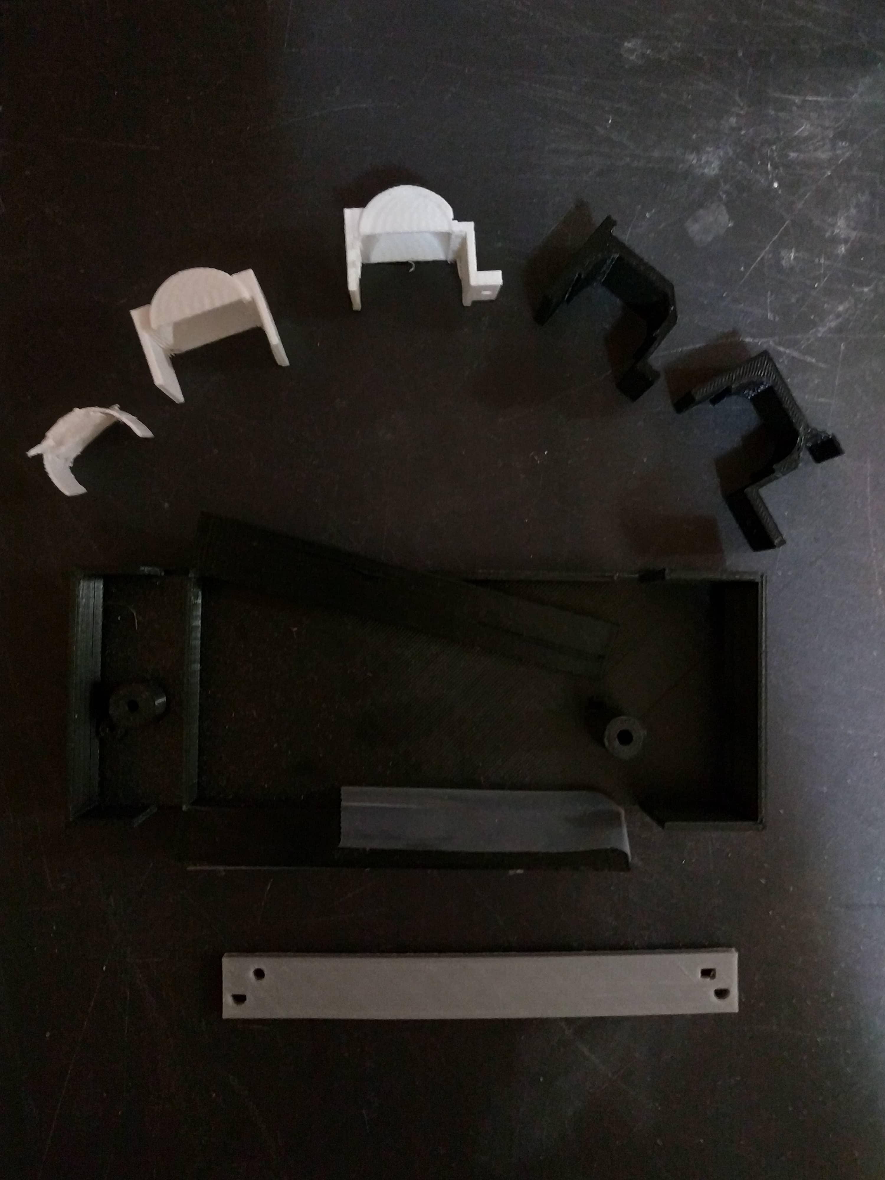 Five iterations of the motor clip design sit on a table above one of the original buggy bases and the plastic rectangle with screw holes in it
