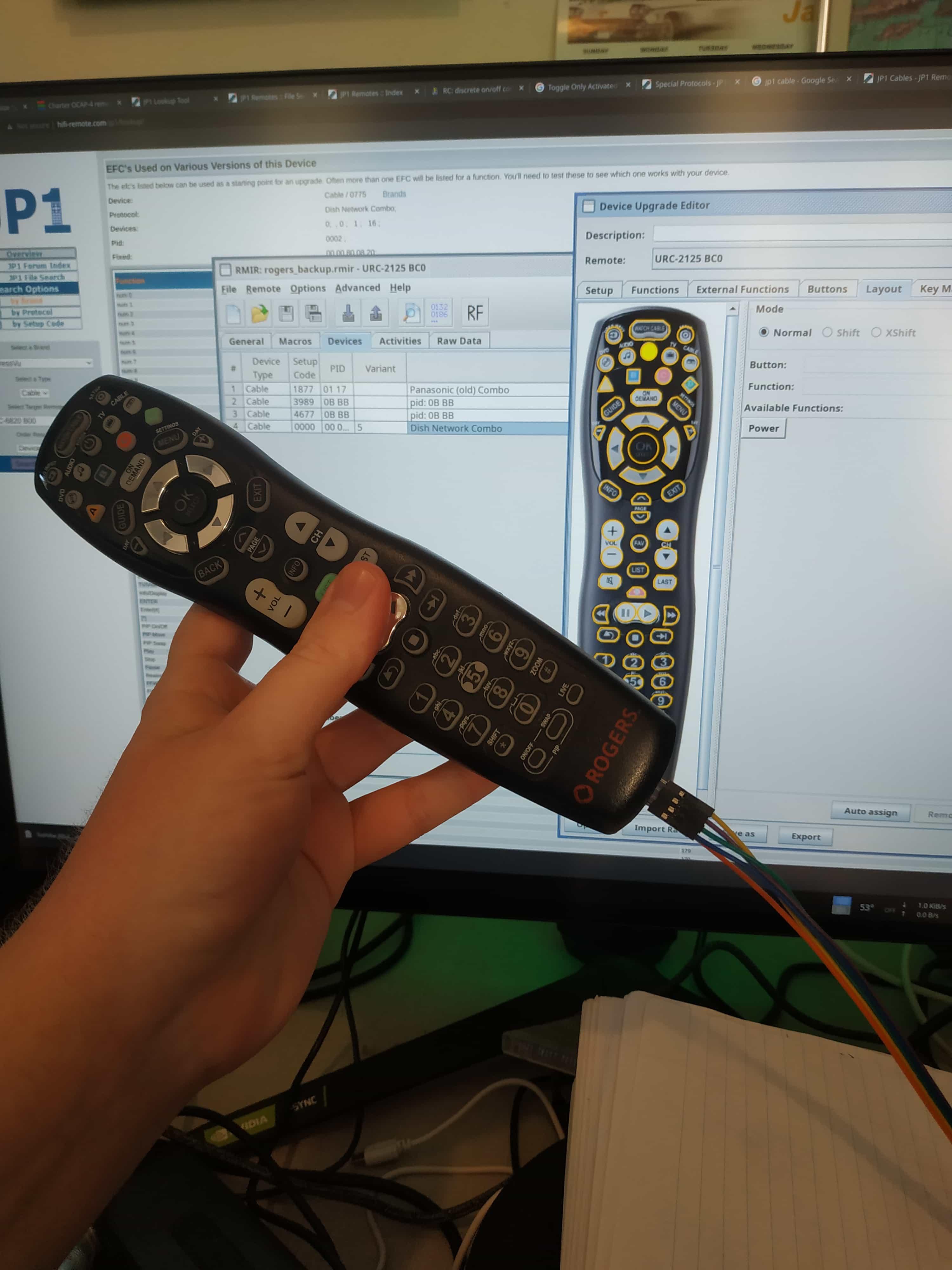 My hand holding a black TV remote with four little wires connected to it. In front of my large computer monitor, which is displaying a picture of the remote on Remote Master