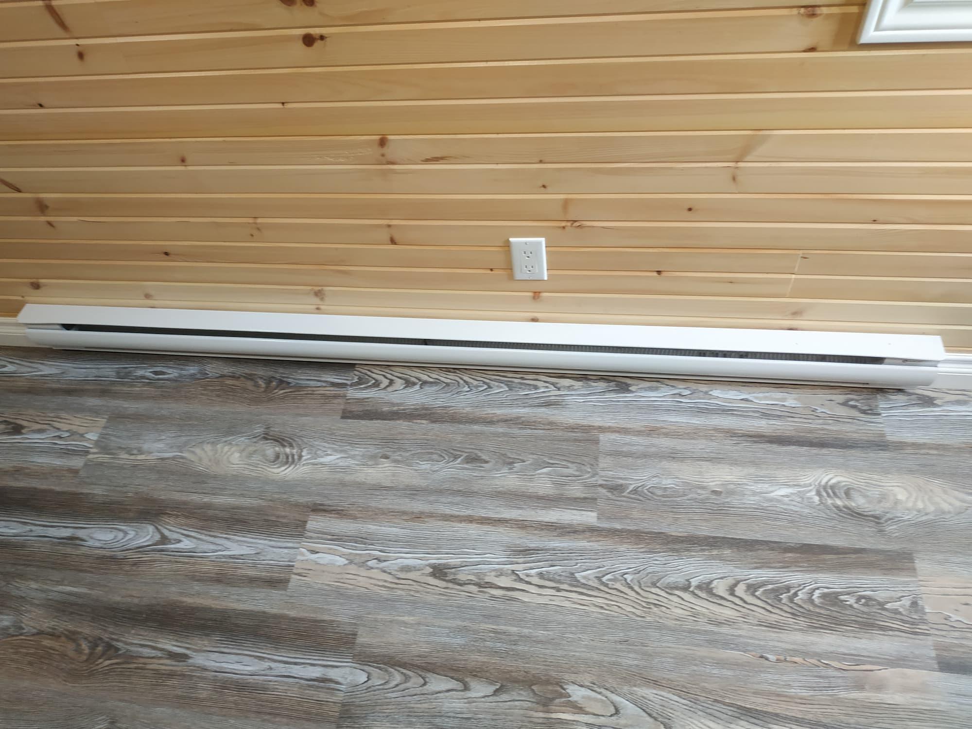 A long white baseboard heater is positioned at the bottom of a pine wall