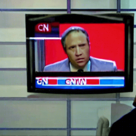 A TV on a wall is tuned to a news broadcast. The anchor looks disturbed, and the text on the screen is unreadable